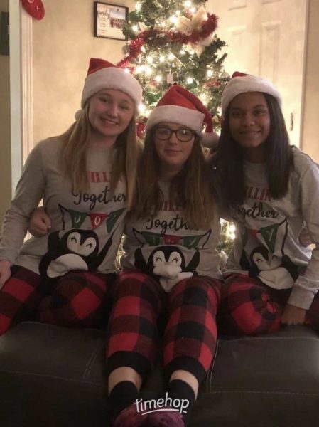 Three kids wearing matching clothes and santa hats, sitting in front of a Christmas Tree.